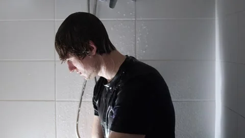Enjoys refreshing shower young man in dark shirt under stream of water tilts hea Stock Footage 315991711