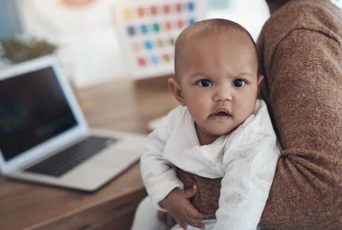 Enough work, when is it playtime. a young woman using a laptop while caring for 스톡 사진