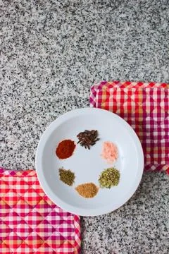 Ensemble of spices in a white dish over a granite countertop. Top down view. Stock Photos
