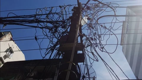 Entangled electric cables from below, electric pole, sunny sky, buildings, bag Stockbeeldmateriaal 77815954