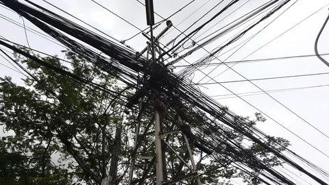 Entangled intersecting electric cables on electric poll, leaves, Vientiane, Laos Видео 75038650