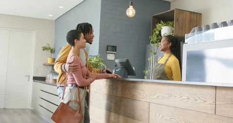 Entering cafe, couple tapping smartphone at reader to pay, barista handing cup, Vídeo Stock 340986804