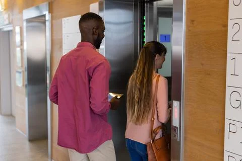 Entering elevator, man holding smartphone and woman pressing button, office Foto stock