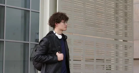 Entering frame, man walking along sidewalk, wearing headphones and carrying Stock Footage 339320636