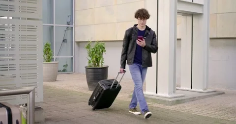 Entering glass walkway, man pulling black suitcase, checking phone for time, Stock Footage 339320595