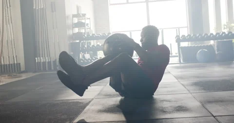 Entering gym causing African American man grabbing medicine ball twisting torso Stock Footage 313957744