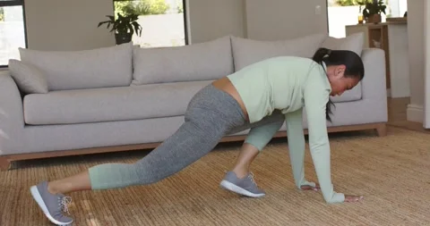 Entering high plank near beige sofa, woman performing knee drives and holding Vídeos de archivo 340972747