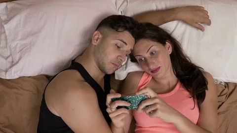 Entertained young couple sitting in bed watching a video on smartphone expres Stock Footage 80177903