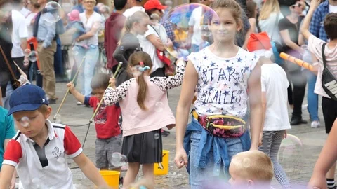 Entertaining children making huge amount of soap bubbles in public city center Stock Footage 89487258