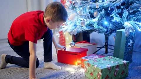 Enthusiastic about opening a gift, the boy admires the decorated Christmas tree. Stock Footage 258582724