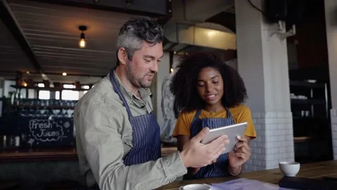 Enthusiastic cafe workers chatting making decisions while scrolling on tablet Stock Footage 138637948