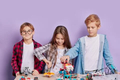Enthusiastic concerned children assembling tech robots, future engineers Stock Photos