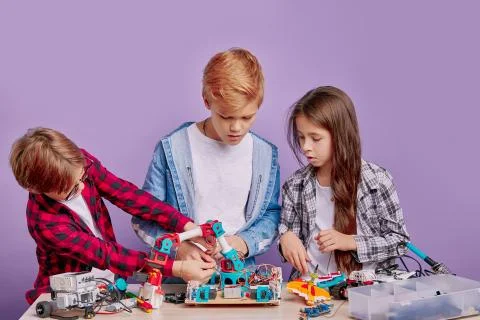 Enthusiastic concerned children assembling tech robots, future engineers Stock Photos