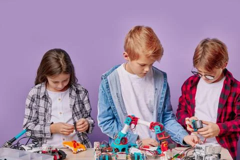 Enthusiastic concerned children assembling tech robots, future engineers Stock Photos