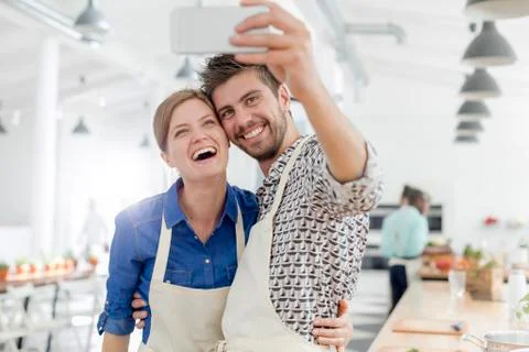 Enthusiastic couple taking selfie with camera phone in cooking class kitchen Stock Photos