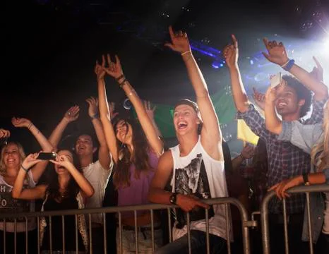 Enthusiastic crowd with arms raised behind railing at concert Stock Photos