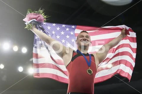 Enthusiastic male gymnast celebrating victory holding American flag on winners Stock Photos