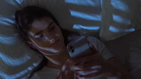 Enthusiastic Pretty Girl Using Mobile Phone while Lying in Bed at Night. Female Stock Footage 125987133