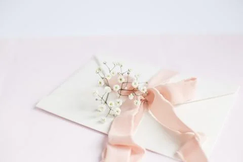 Envelope on a white-pink background with peach silk ribbon and pink flowers.  Stock Photos