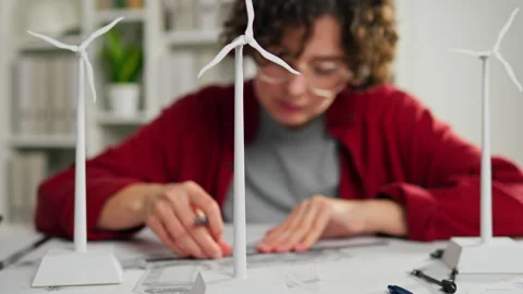 An environmental designer drafting plans near miniature wind turbines at a w Video stock 323710735