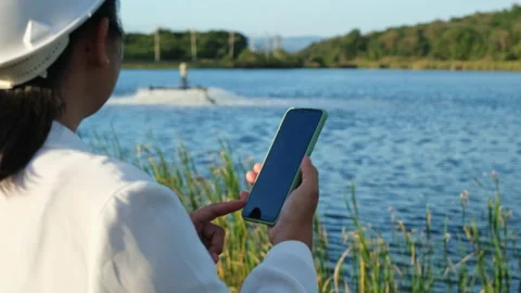 Environmental engineer uses a mobile phone to operate an oxygen turbine aerator. Stock Footage 229704450