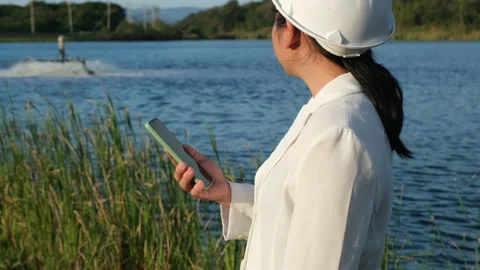 Environmental engineer uses a mobile phone to operate an oxygen turbine aerator. Stock Footage 229704803