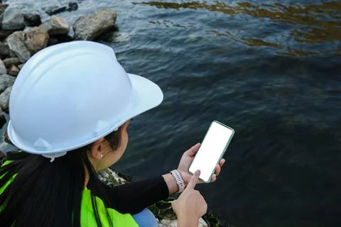 Environmental engineer uses a mobile phone to record water analysis data in dam. Foto stock