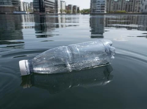 Environmental pollution - plastic bottle floating in sea water in urban city. Stock Photos