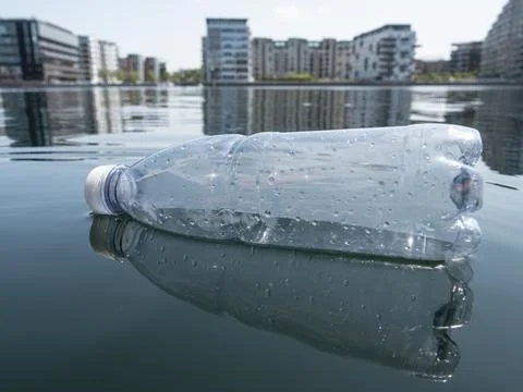 Environmental pollution - plastic bottle floating in sea water in urban city. Stock Photos