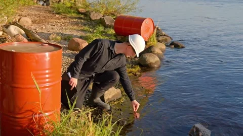 Environmental worker testing for water pollution from chemical waste barrels Stock Footage 321865671