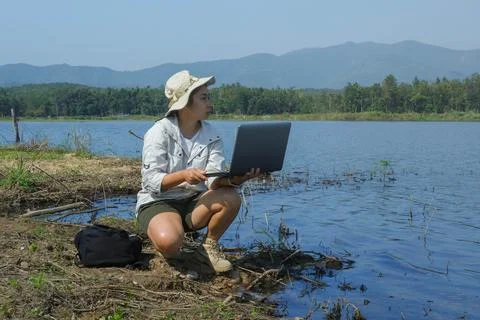An environmentalist uses a laptop to record pathogen analysis in natural water. Stock Photos