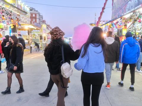 Eomen walking while eating a pink cotton candy at night in a fair Stock Photos