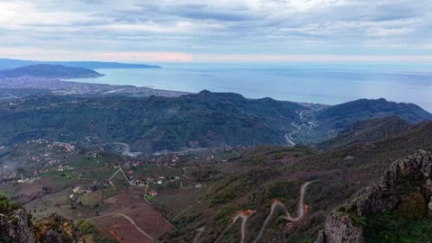 Epic Drone Flying Between Sharp Peaks Revealing Distant Stormy Coastal City, 4K Video stock 335076040