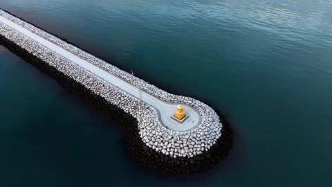 Epic drone flyover of yellow lighthouse above turquoise ocean and snowy rock Video stock 326132407