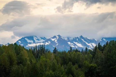 Epic mountain range with peaks, forest, and clouds in background of landscape Stock Photos