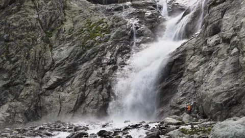 Epic view of a powerful waterfall and a tiny man at its foot slow motion Stock Footage 256806396