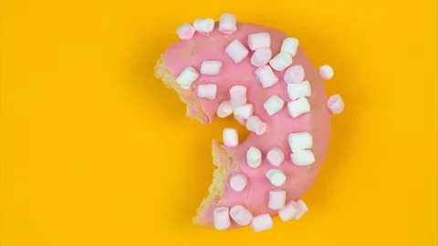 Eqating pink donut on a yellow background. Bite by bite Stock Footage 128922961