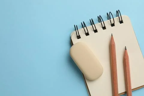 Eraser, pencils and notepad on light blue background, top view. Space for tex Stock Photos