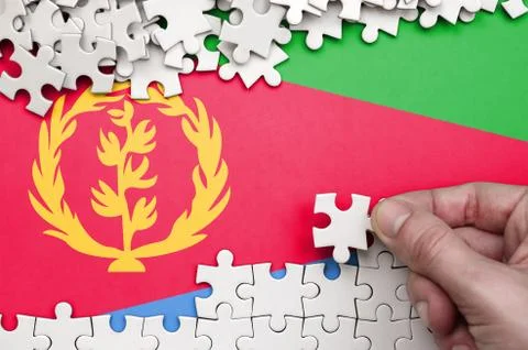 Eritrea flag  is depicted on a table on which the human hand folds a puzzle o 写真素材