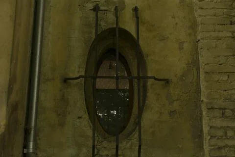 Eroded oval window framed by iron bars against urban decay backdrop Stock Photos