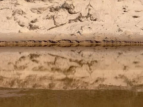 Eroded Sandy Riverbank Reflected in Calm Water Texture Stock Photos