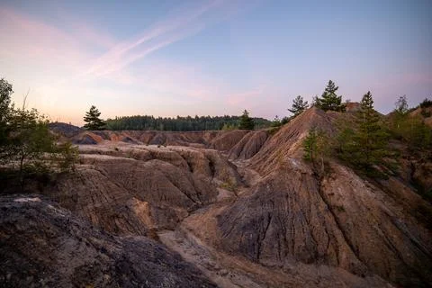 Eroded soil quarry ravine with forest on its edge at summer evening Stockfoto's