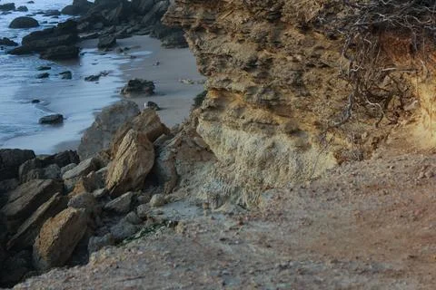Eroding cliff face overlooking sandy beach and ocean waves Stock Photos