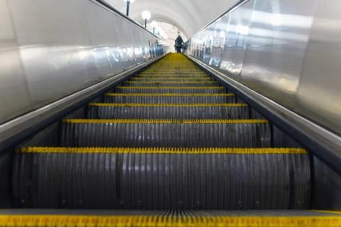 Escalator view from below. At the top are silhouettes of people. Steps with y Foto stock