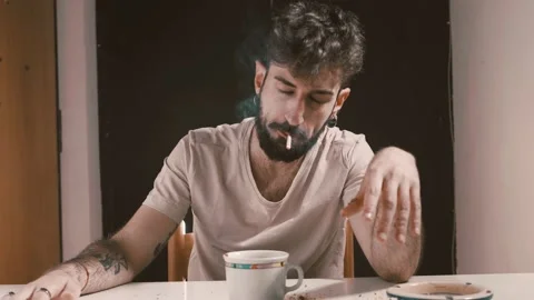Escape from reality - young addict sitting at the table smokes greedily a joint  Stock Footage 197813489