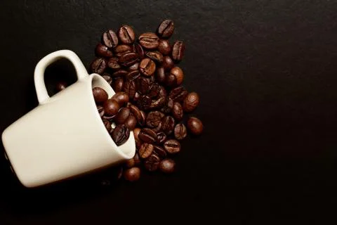 Espresso cup with coffee beans inside fell on the dark textured table Stock Photos