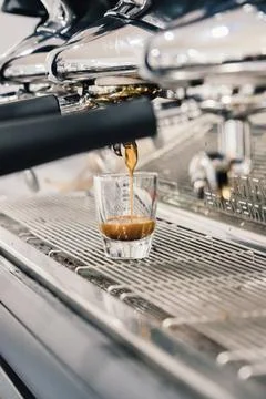 Espresso dripping from portafilter of coffee machine into glass cup Stock Photos