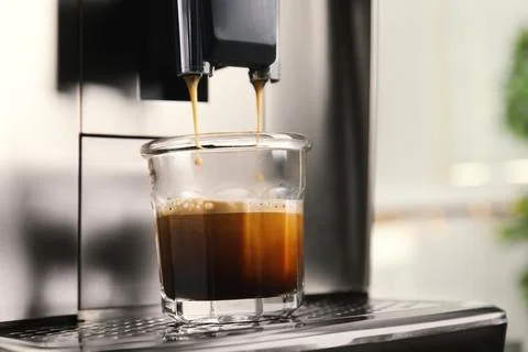 Espresso machine pouring coffee into glass against blurred background, closeu Stock Photos