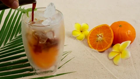 Espresso Pouring Into Iced Orange Glass On Palm Leaf Against Plumeria Flowers. Vídeo Stock 196974553