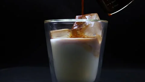 Espresso shot pouring into iced cube milk glass while rotating. Vidéo 250217092